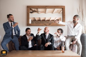 On the wedding day, at Domaine Mas du Conte, the groom and his best men enjoy a moment together, sharing a glass of whiskey while seated on a cozy couch.